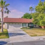 Real estate single-story house with red tile roof, green lawn, and palm trees.