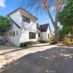 Real estate house with white siding, large windows, driveway, garage, and trees.