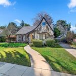 Real estate house with sloped roof, ivy walls, hedges, flower beds, and front yard.
