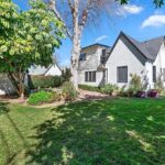 Real estate white house with sloped roof, garden, grass, and trees.