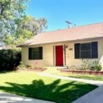 Real estate single-story house with red door, blue shutters, and green lawn.