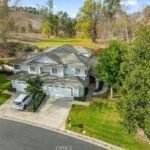 Aerial view of real estate two-story house with gray roof, trees, driveway, and car.