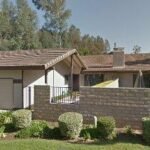 Real estate house with driveway, tiled roof, stone wall, and palm trees.